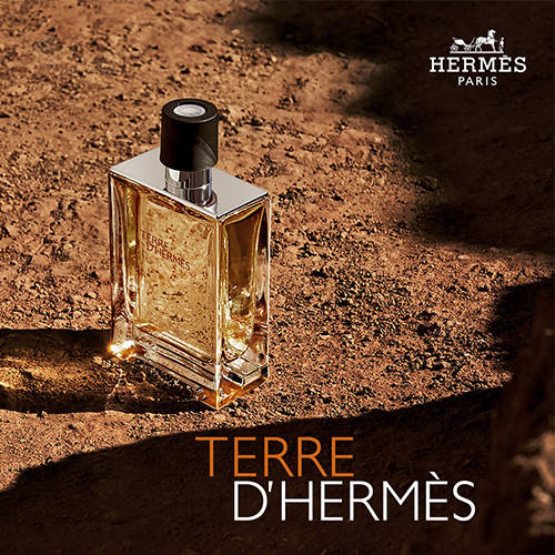 Perfume Terre d’Hermès em frasco âmbar sobre solo terroso, inspirado em elementos minerais.